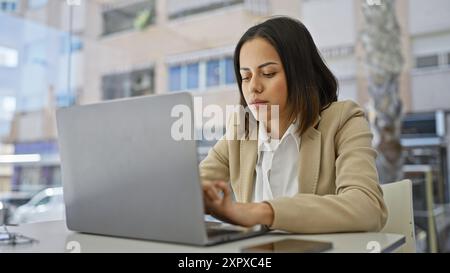 Giovane donna concentrata che utilizza un notebook in un ambiente di lavoro moderno, dimostrando professionalità e serietà Foto Stock