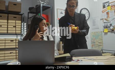 Due donne, probabilmente detective, sono occupate in un ufficio, una al telefono e l'altra prendono appunti tra i file delle indagini. Foto Stock