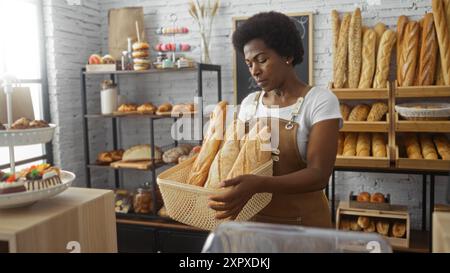 Donna che lavora in un panificio con un cesto di pane fresco con scaffali di dolci e pani sullo sfondo Foto Stock
