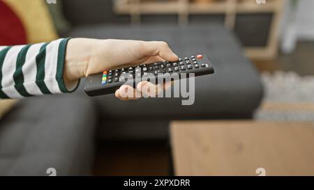 Un primo piano di una mano di una donna che tiene in mano il telecomando della tv, suggerendo il tempo libero in un accogliente soggiorno. Foto Stock