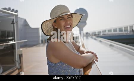 Una donna sorridente in cappello da sole ama divertirsi su un ponte delle navi da crociera che si affaccia sull'oceano. Foto Stock