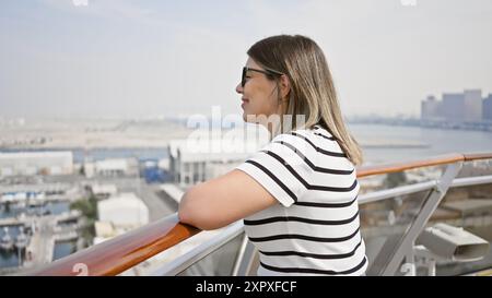 Una giovane bruna si gode un momento di relax sul ponte di una nave da crociera, guardando l'oceano sotto un cielo limpido. Foto Stock