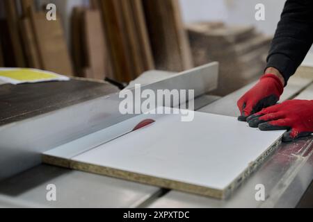 Primo piano del lavoratore tagliando e planando con cura pezzi di legno per mobili nell'industria del legno Foto Stock