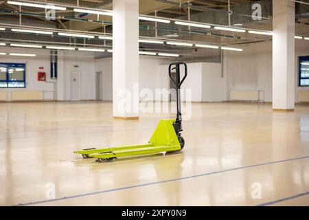 Martinetto manuale o carrello elevatore a forche di colore verde utilizzato su un pavimento vuoto e illuminato in fabbrica, senza persone. Foto Stock