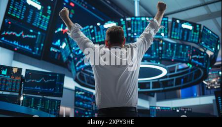 Un uomo d'affari entusiasta si alza la mano e si fa strada festeggiando un affare di successo. Manager di Borsa felice dopo la giornata degli investimenti. Broker in White Shirt vince un contratto redditizio. Vista posteriore Foto Stock