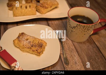 Sfogliare con mele su un piatto bianco con una tazza di caffè e un piccolo regalo sul bordo del piatto Foto Stock