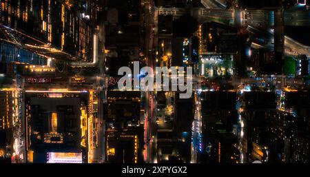 Lo scatto notturno in elicottero cinematografico si muove diagonalmente sopra il New York City Avenue Grid System. Foto dall'alto verso il basso delle strade congestionate, delle strade, delle automobili, della vita notturna e dei grattacieli alti e moderni Foto Stock
