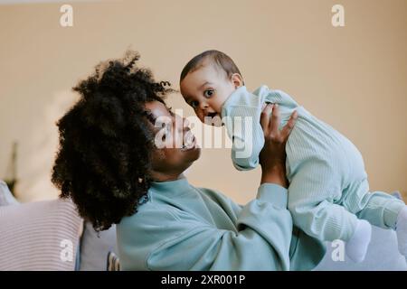 Mamma afroamericana che ammira il suo bambino e gioca con lui mentre il bambino guarda la macchina fotografica Foto Stock