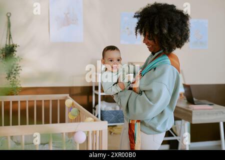 Madre afroamericana sorridente che tiene in fionda il suo bambino curioso e adorabile Foto Stock