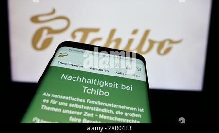 Telefono cellulare con sito web della società tedesca di vendita al dettaglio di caffè Tchibo GmbH davanti al logo aziendale. Mettere a fuoco in alto a sinistra sul display del telefono. Foto Stock