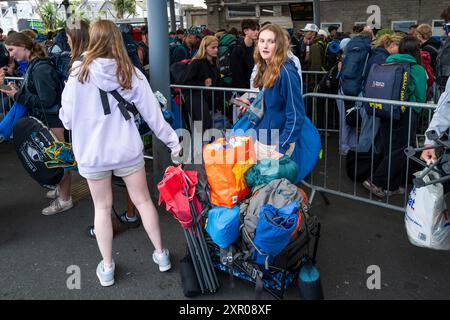 Alcuni dei 1400 giovani entusiasti fanno la fila pazientemente dopo essere arrivati su un treno alla stazione ferroviaria di Newquay per il Boardmasters Festival di Newquay Foto Stock