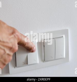 Un portachiavi bianco su una parete bianca. La mano accende la luce Foto Stock