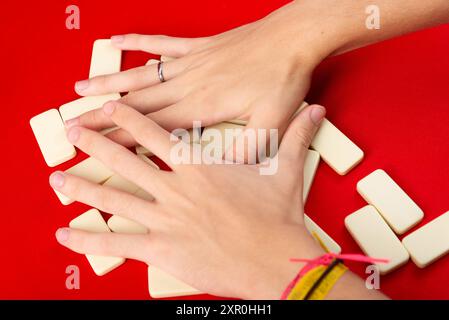 Mani maschili che mescolano domino. pezzi acrilici. Isolato su sfondo rosso. Foto Stock