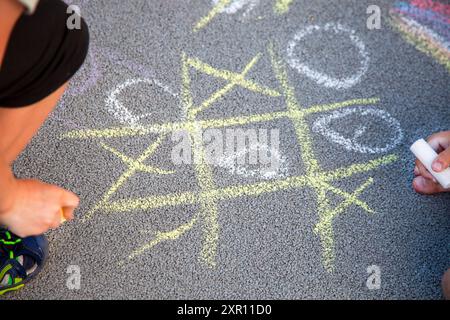 Il TIC-tac-toe di gioco è disegnato sull'asfalto. I bambini giocano all'aperto. Disegno con gesso colorato del marciapiede. Attività di gioco all'aperto Foto Stock