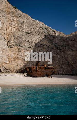 Un naufragio arrugginito sulla spiaggia sabbiosa di Navagio Beach con acque cristalline e scogliere sotto un cielo luminoso a Zante, in Grecia. Scatto verticale. Foto Stock