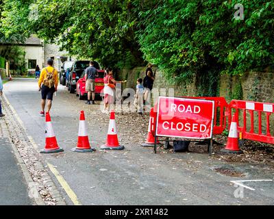 Un gruppo di persone si riunisce vicino a un cartello stradale chiuso e alle barriere, deviando il percorso attraverso un quartiere panoramico. Foto Stock