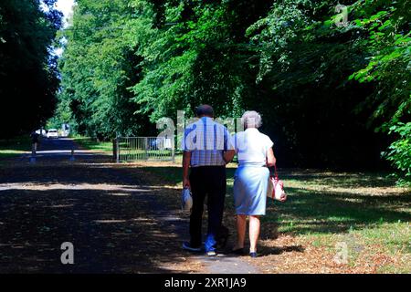Una coppia anziana che cammina lungo un vicolo ombreggiato in una giornata di sole. Presa agosto 2024. Estate Foto Stock