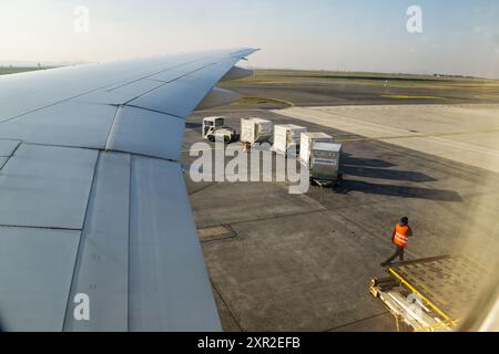 02MAR2023, SSR AIRPORT, MAURITIUS - Vista dell'ala di un aereo parcheggiato e dei container sull'asfalto dall'oblò durante l'assistenza a terra Foto Stock