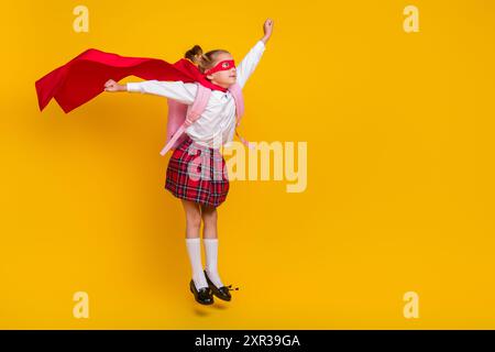 Ritratto completo del corpo dell'uniforme del costume da supereroe piccolo scolaro salta uno spazio vuoto isolato su sfondo giallo Foto Stock