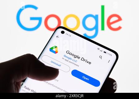 Primo piano dello schermo di uno smartphone che visualizza l'app Google Drive con il logo Google sullo sfondo, che illustra la connessione tra Google Drive e G. Foto Stock