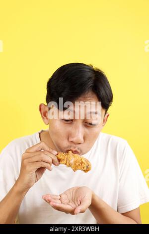 Uomo indonesiano che mangia il bastoncino di pollo fritto croccante su sfondo giallo Foto Stock