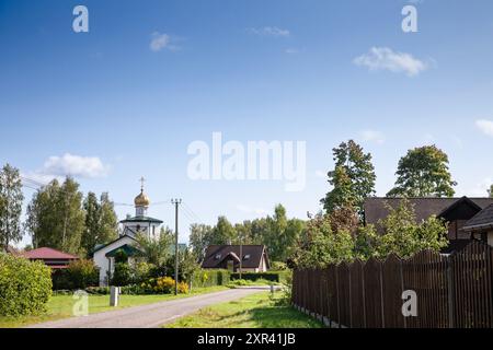 Una pittoresca scena di un villaggio russo o lettone nell'Europa orientale, caratterizzata da un'architettura tradizionale e da una chiesa ortodossa russa. Foto Stock