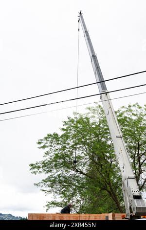 Costruzione di abitazioni residenziali, consegna di legname di sollevamento con gru a braccio, travi di sostegno in legno, operaio che assiste nel posizionamento Foto Stock