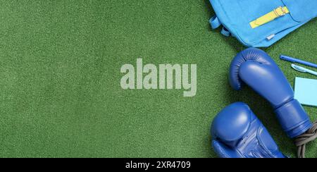 Zaino con guanti da boxe e cancelleria scolastica su erba verde. Banner per il design Foto Stock