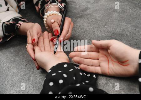 L'indovino che legge le righe sul palmo della donna al tavolo grigio, primo piano. Chiromancy Foto Stock