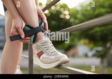 Donna che indossa pesi alla caviglia all'aperto, primo piano Foto Stock