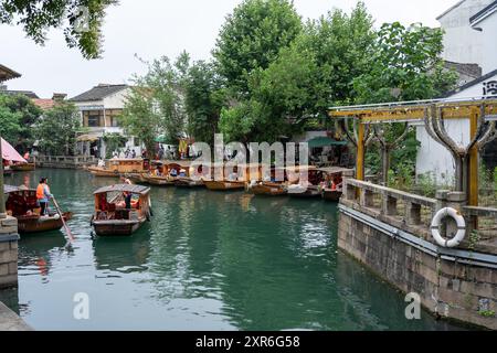 Suzhou, Cina - 11 giugno 2024: Un canale a Suzhou, Cina, fiancheggiato da case tradizionali, con barche di legno ancorate lungo il bordo dell'acqua. Foto Stock