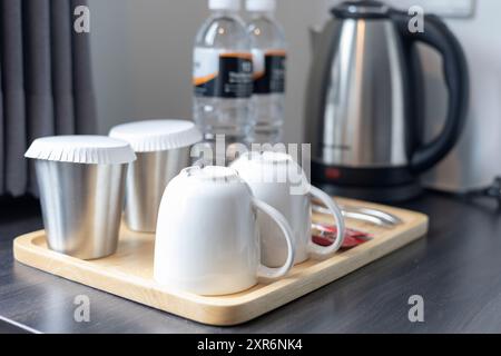 Cucina moderna: Tazze e tazze disposte in modo ordinato su un vassoio di legno accanto a un bollitore e bottiglie d'acqua color argento, per una bevanda pulita e organizzata Foto Stock