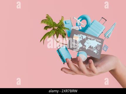 Una mano che tiene in mano una carta di credito circondata da oggetti di viaggio come una palma, bagagli, aeroplani e accessori da spiaggia su sfondo rosa. Conce Foto Stock