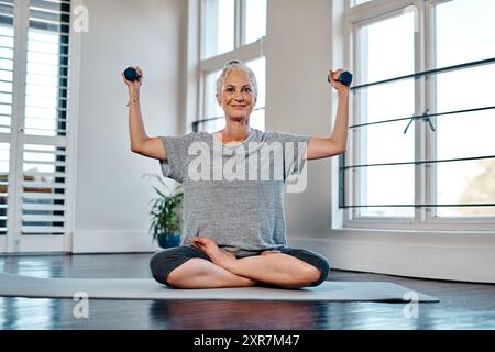 Donna anziana, ritratti e manubri in studio domestico su tappetino yoga per esercizio fisico e benessere. Buona pratica fisica e fisiologica per la riabilitazione e. Foto Stock