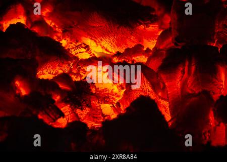 Una dispersione di carboni ardenti si illumina al buio della stufa. Mostrano la struttura stratificata del legno. Primo piano. Foto Stock