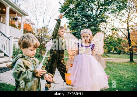 Tre bambini in costumi da fata e dinosauro che giocano all'aperto Foto Stock
