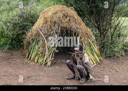 Capanna e freccia di preparazione per arco, tribù Hadzabe, cacciatori-raccoglitori, gruppo etnico indigeno, reparto Baray, S.W. distretto di Karatu della regione di Arusha. Tanzano Foto Stock