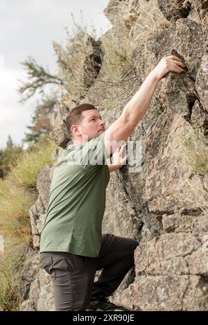 Uomo che sale sul fianco di una grande roccia Foto Stock