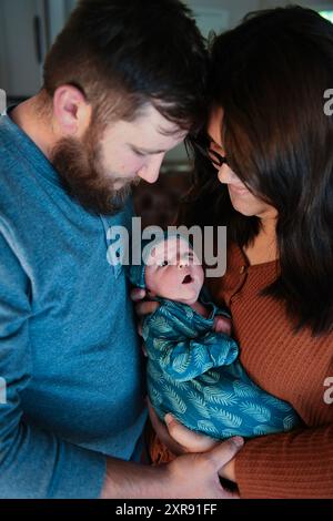 I genitori tengono in braccio con amore il loro neonato con motivi a foglia blu Foto Stock