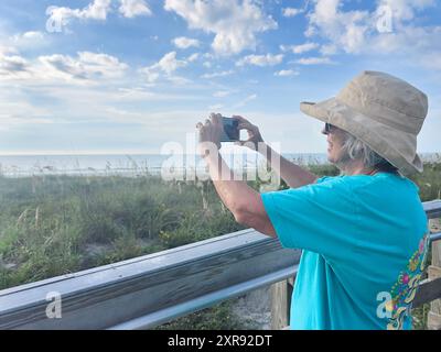 Donna con cappello che scatta una foto in una passeggiata panoramica lungo la costa Foto Stock