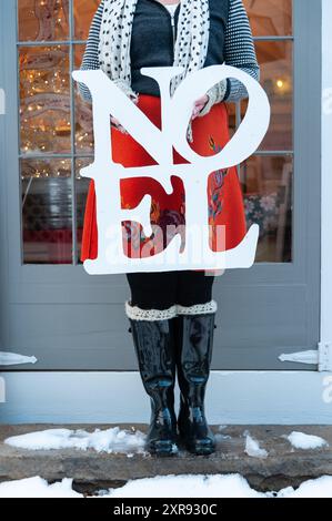 Persona con stivali invernali con un cartello "NOEL", in piedi all'esterno Foto Stock