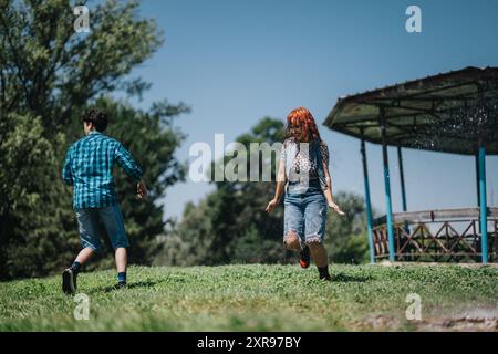 Gruppo di amici che si divertono con l'acqua alla fontana in un parco soleggiato Foto Stock