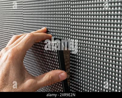 Primo piano della mano di un uomo che installa un modulo LED quadrato al suo posto sulla superficie di un grande schermo LED. Foto Stock