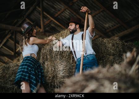 Giovane coppia in un fienile rustico appoggiata a balle di fieno con cappelli da cowboy Foto Stock