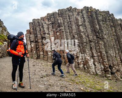 La gente cammina accanto alle colonne di pietra basaltica. Il Selciato del gigante e la costa del Causeway sono un’area di importanza geologica globale sulla costa marittima dell’Irlanda del Nord. Le 40.000 colonne di pietra basaltica lasciate da eruzioni vulcaniche 60 milioni di anni fa hanno attirato milioni di turisti nel corso degli anni. Il Selciato del gigante è l'attrazione turistica più popolare in tutta l'Irlanda, Nord o Sud. Foto Stock