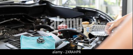 Una persona sta versando acqua nel radiatore di un'auto. La persona sta cercando di raffreddare il motore dell'auto. La vettura si sta surriscaldando nel serbatoio del parabrezza all'interno Foto Stock