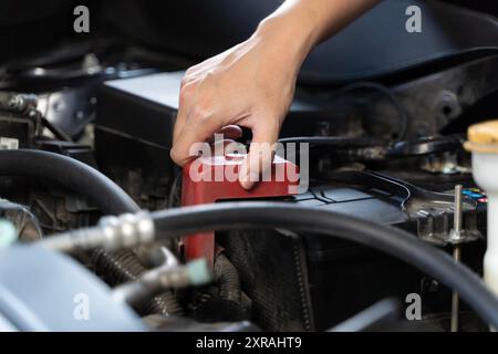 Una donna che ispeziona la batteria di un'auto, che si trova di fronte all'auto con il cofano aperto, e guarda la batteria. Una batteria scarica può causare Foto Stock