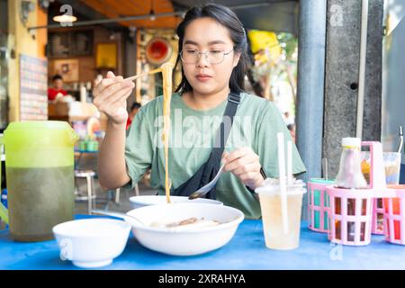 Le donne asiatiche usano la bacchetta mangiando deliziosi spaghetti in ciotola bianca , concentrata sulla noodle. Mangiare azione con il concetto di cibo asiatico. Utilizzando una bacchetta contenente no Foto Stock