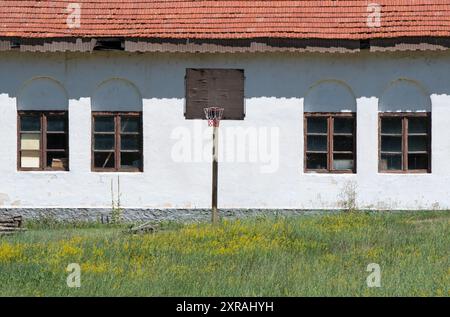 Vecchia architettura di edifici abbandonati: Cortile scolastico con palo da pallacanestro e rete, cornici per finestre simmetriche. Foto Stock