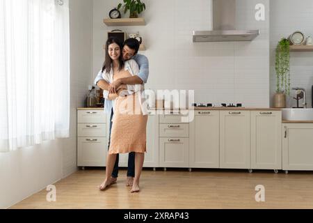 Allegri marito e moglie europei millenari si divertono e ballano negli interni della cucina moderna. Coppia di famiglie ad un appuntamento romantico domestico, intrattenimento Foto Stock